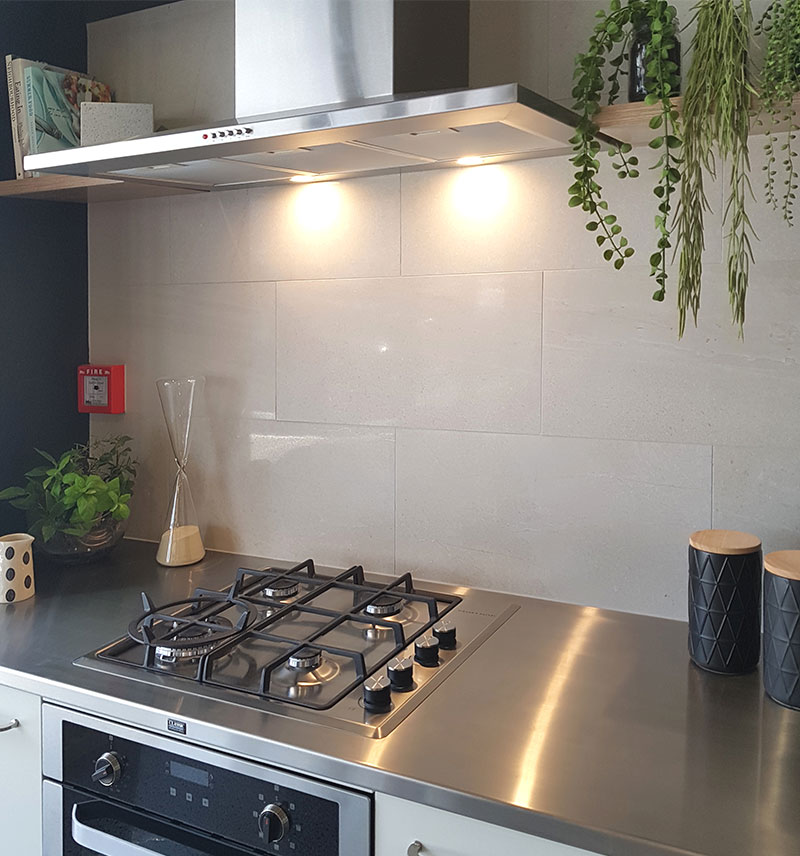 large white tile wall in kitchen above a stainless steel bench and gas hob