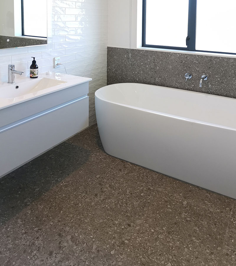 bathroom wit h sink and bathtub tiled in dark charcoal floor, bath backing, and white wall